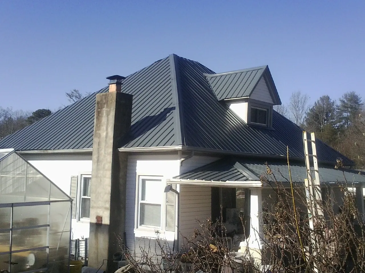 Dark blue standing seam metal roof on a white farmhouse with dormer — Slate & Tile Roof Repair by Roofing Brothers in Devens