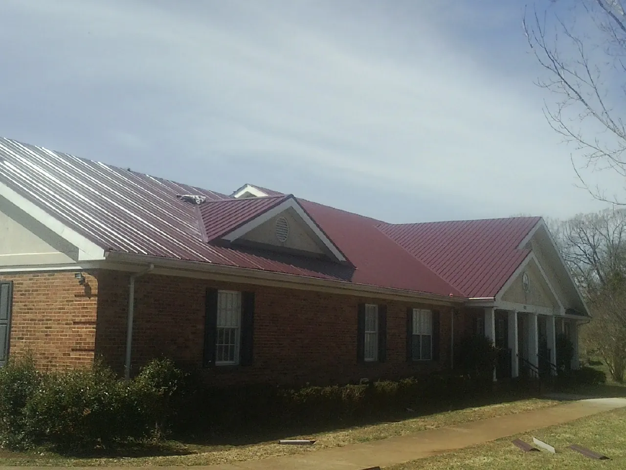 Red metal roof with gabled entries on a long brick building, from a Hail Damage Roof Repair job in Devens