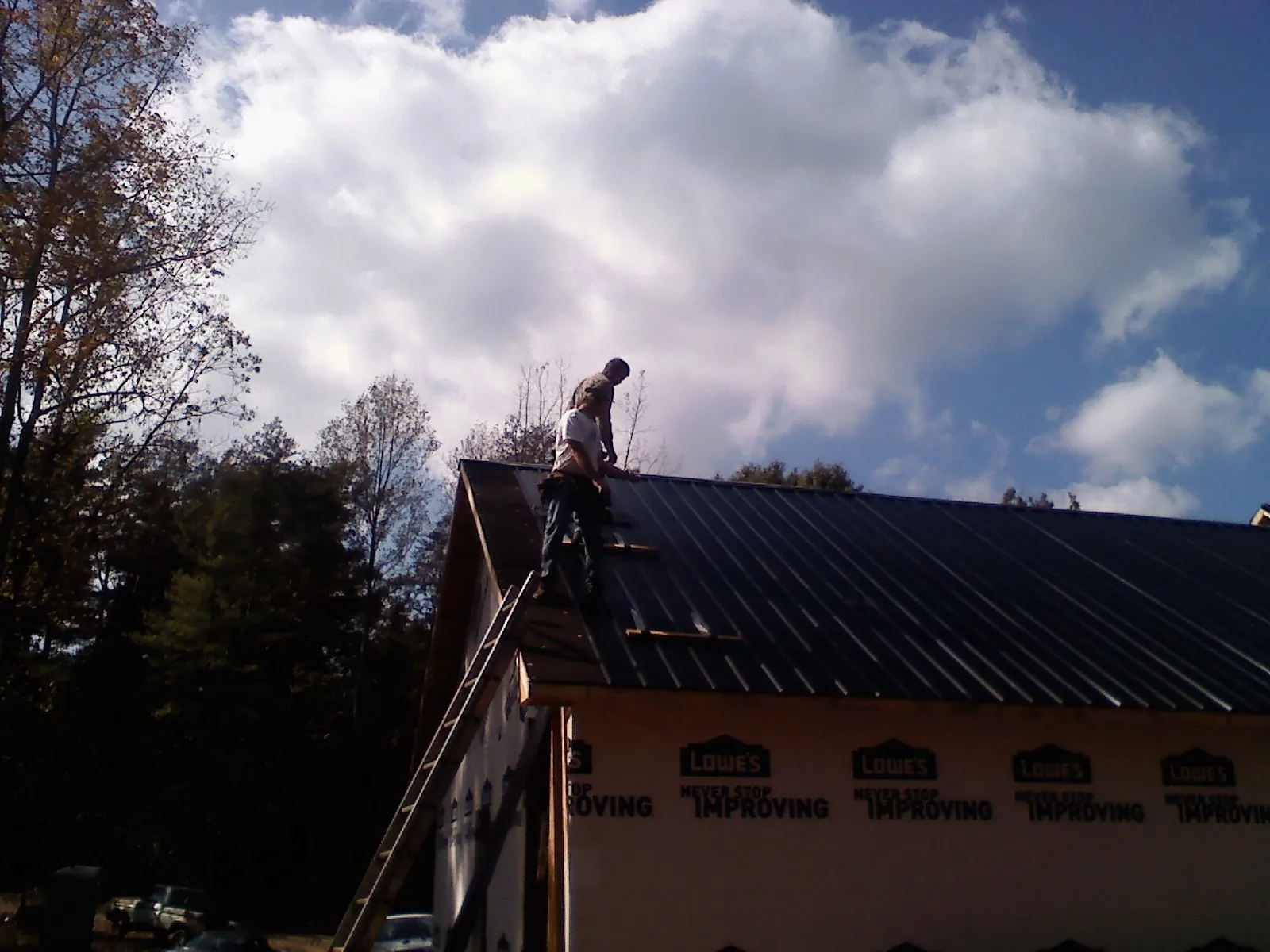 Roofer fastening dark metal panels high against a cloudy sky, from a Roof Inspection job in Devens