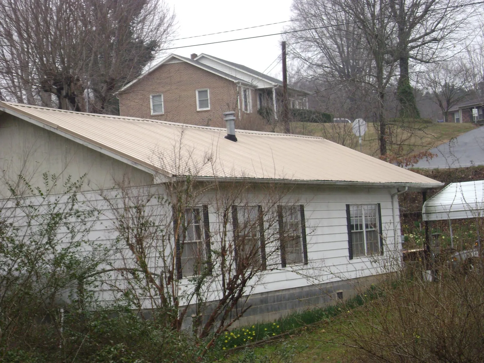 Tan metal roof on a white sided house set into a hillside — Commercial Roofing by Roofing Brothers in Devens