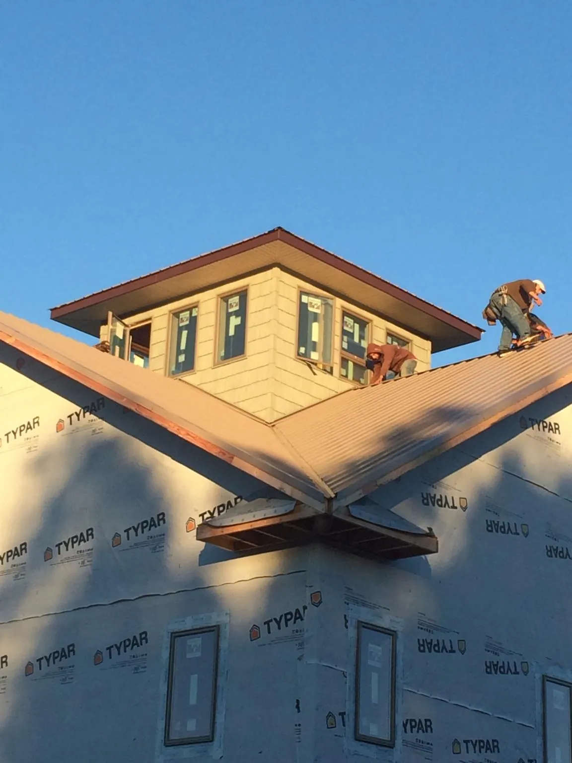 Roofers working around a rooftop cupola on a new metal roof at sunset — Roof Waterproofing in Devens by Roofing Brothers